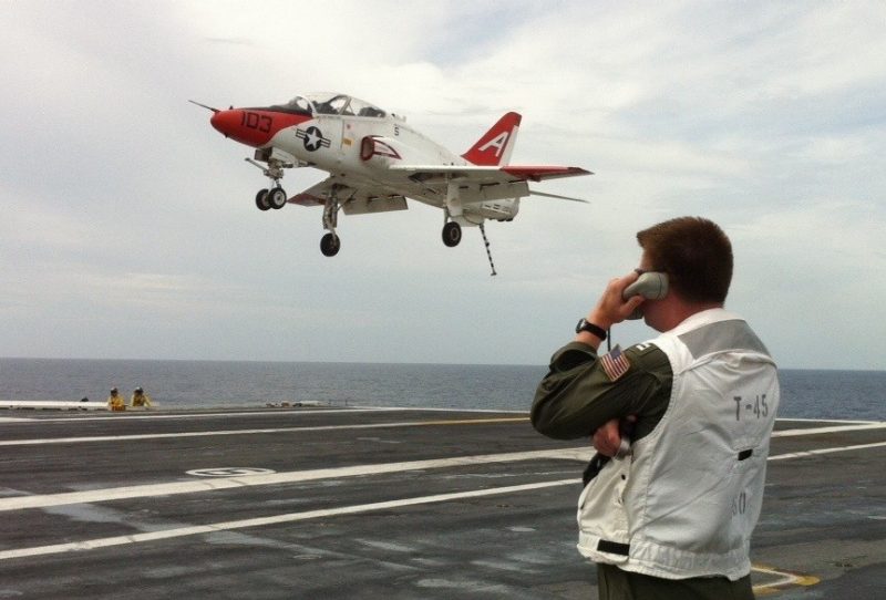 A Boeing T-45C Goshawk flies during a carrier landing with Lt. Michael Renard, U.S. Navy, Virginia Tech Corps of Cadets Class of 2004 in the foreground.